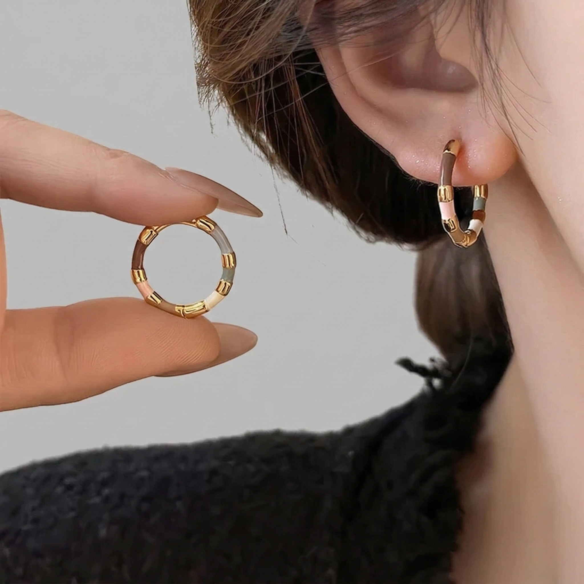 Woman wearing pastel enamel hoop earrings while holding matching earring
